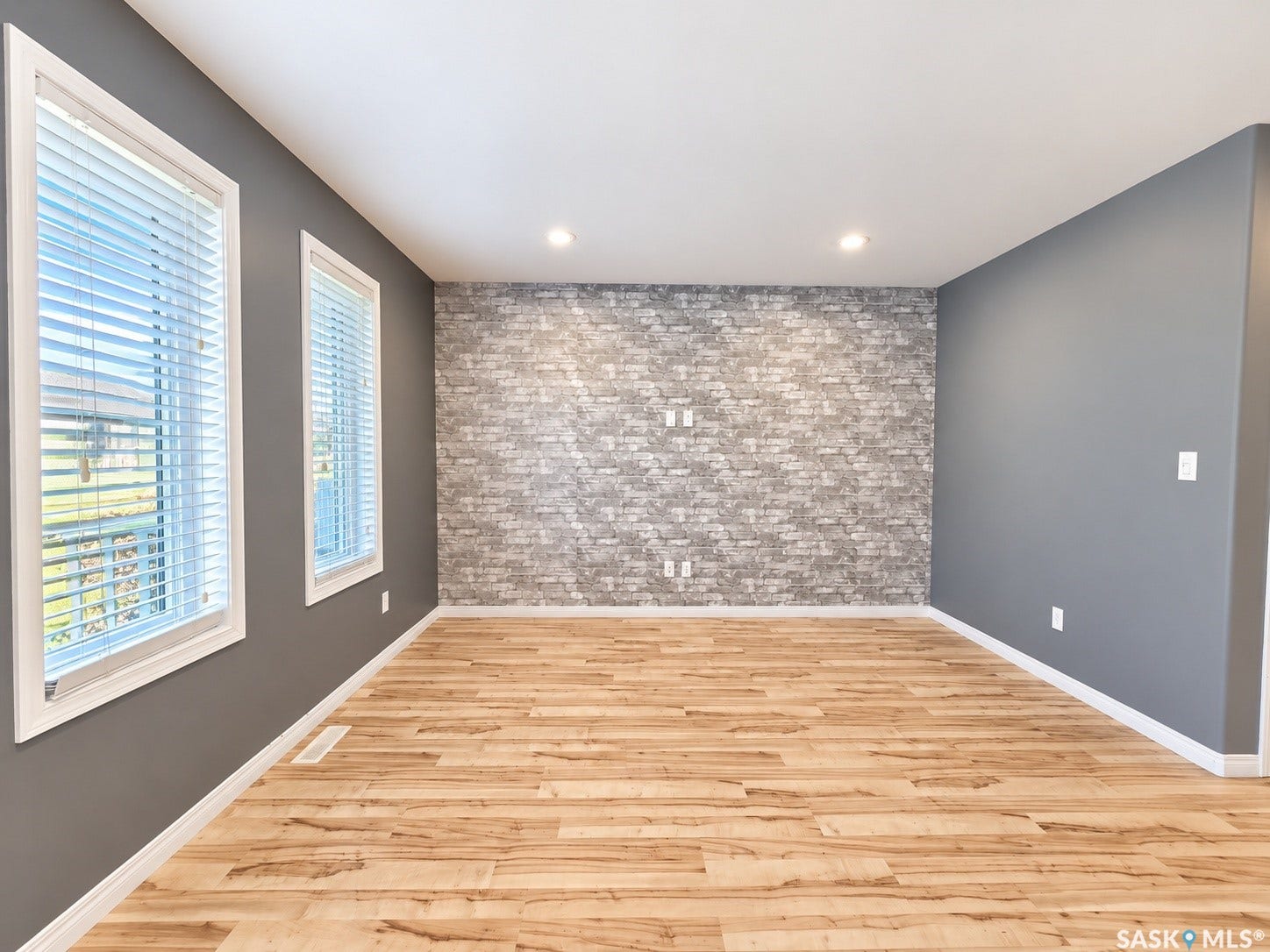 Accent wall with a gray brick pattern, wood-finish flooring, recessed lighting, and dual windows with blinds