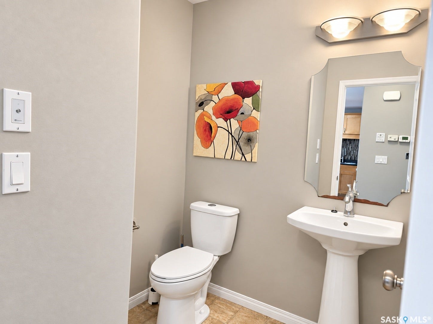 Pedestal sink with chrome faucet, wall-mounted mirror, and overhead vanity lighting