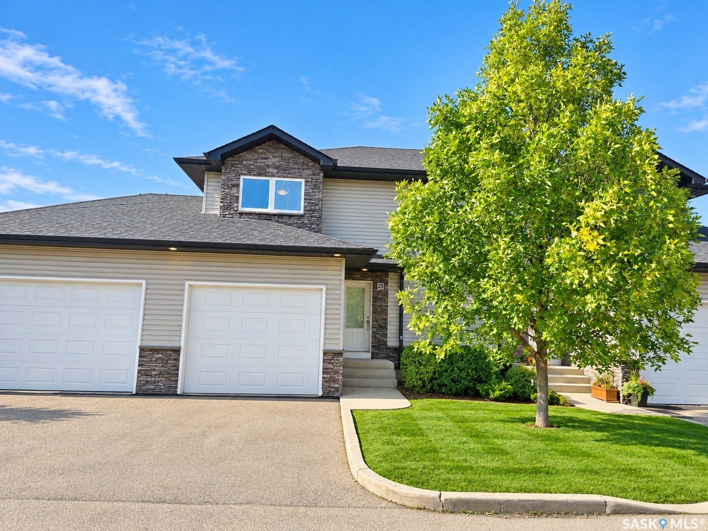 Exterior featuring stone accents, horizontal siding, dual garage doors, a concrete driveway, and a front lawn with mature tree