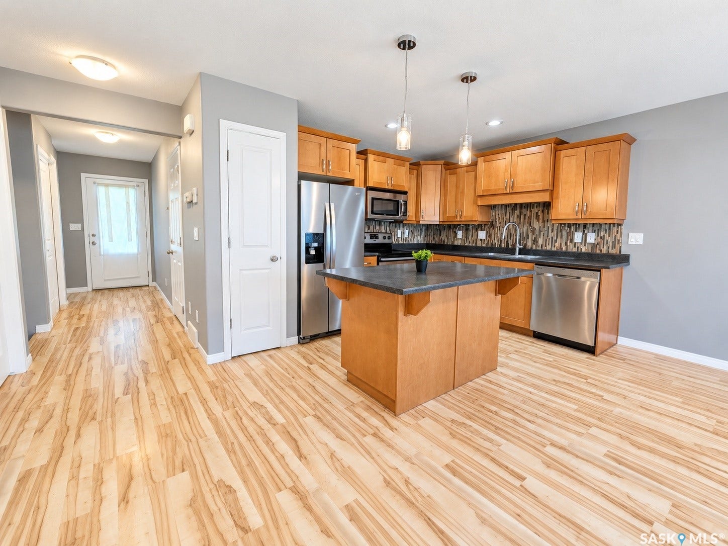 Well-appointed kitchen featuring wood-finish cabinetry, stainless steel appliances, a center island with a dark countertop, and a mosaic tile backsplash