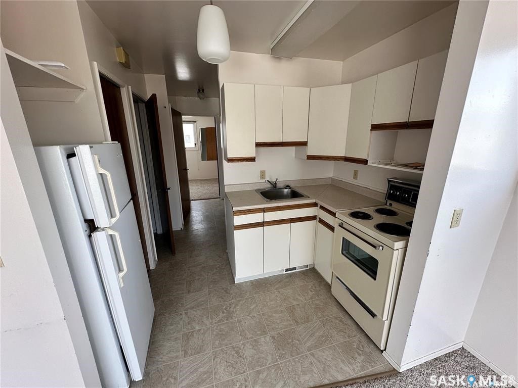 Compact kitchen with white cabinetry, a built-in stainless steel sink, a refrigerator, and an electric range