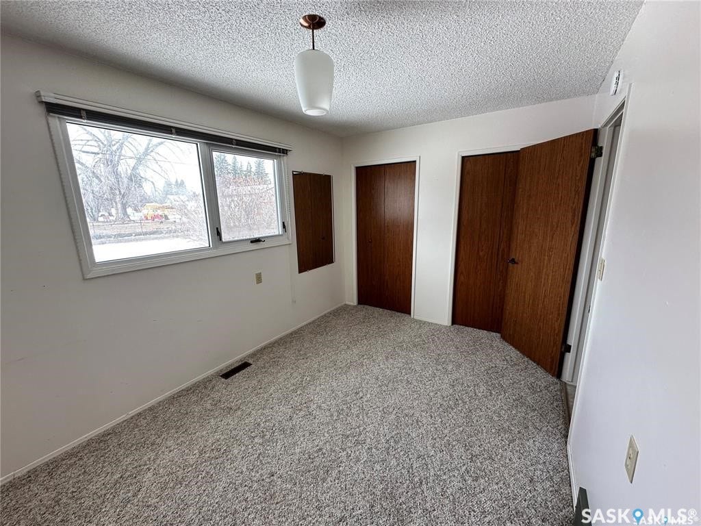 Wide window with white trim, textured ceiling, two wood-finish bi-fold closet doors, and neutral carpeting