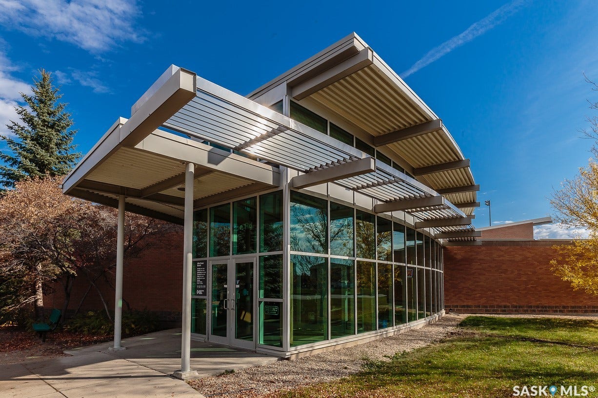 Contemporary architectural design featuring extensive glass curtain walls, a covered entrance, and a slatted metal awning system