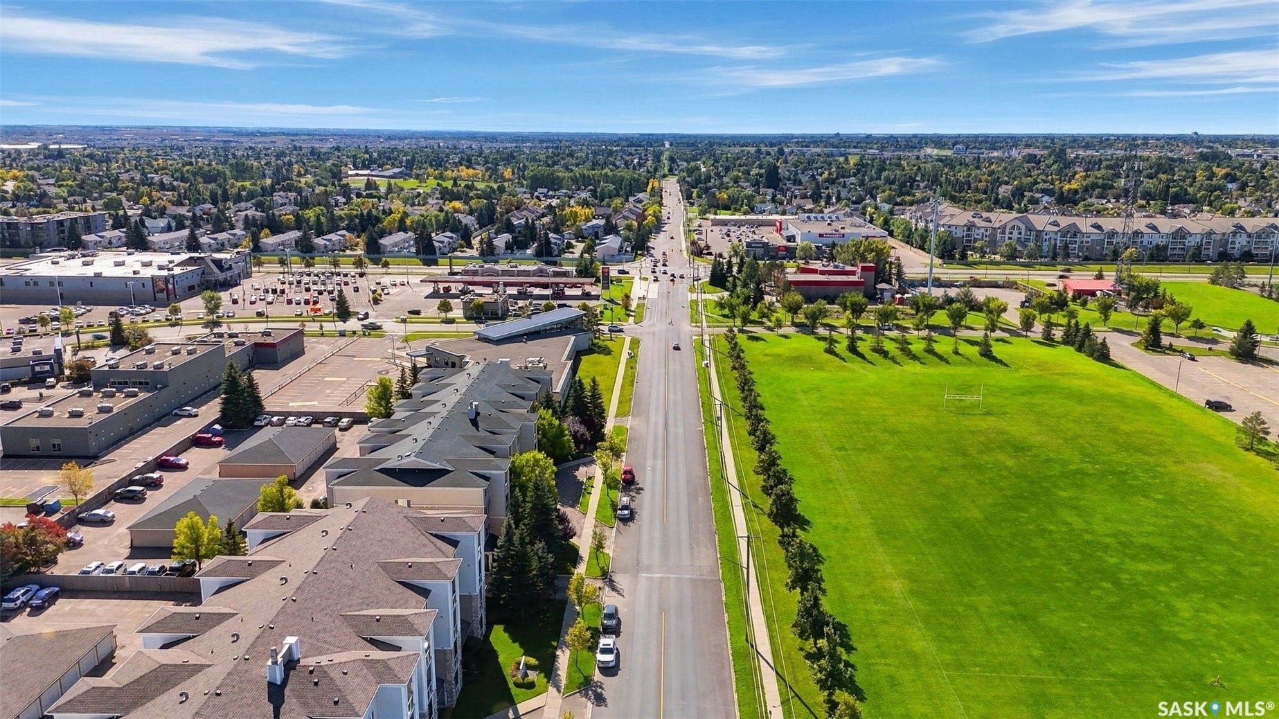 Expansive green spaces and mature trees border a wide road, with commercial and residential structures visible in the surrounding area