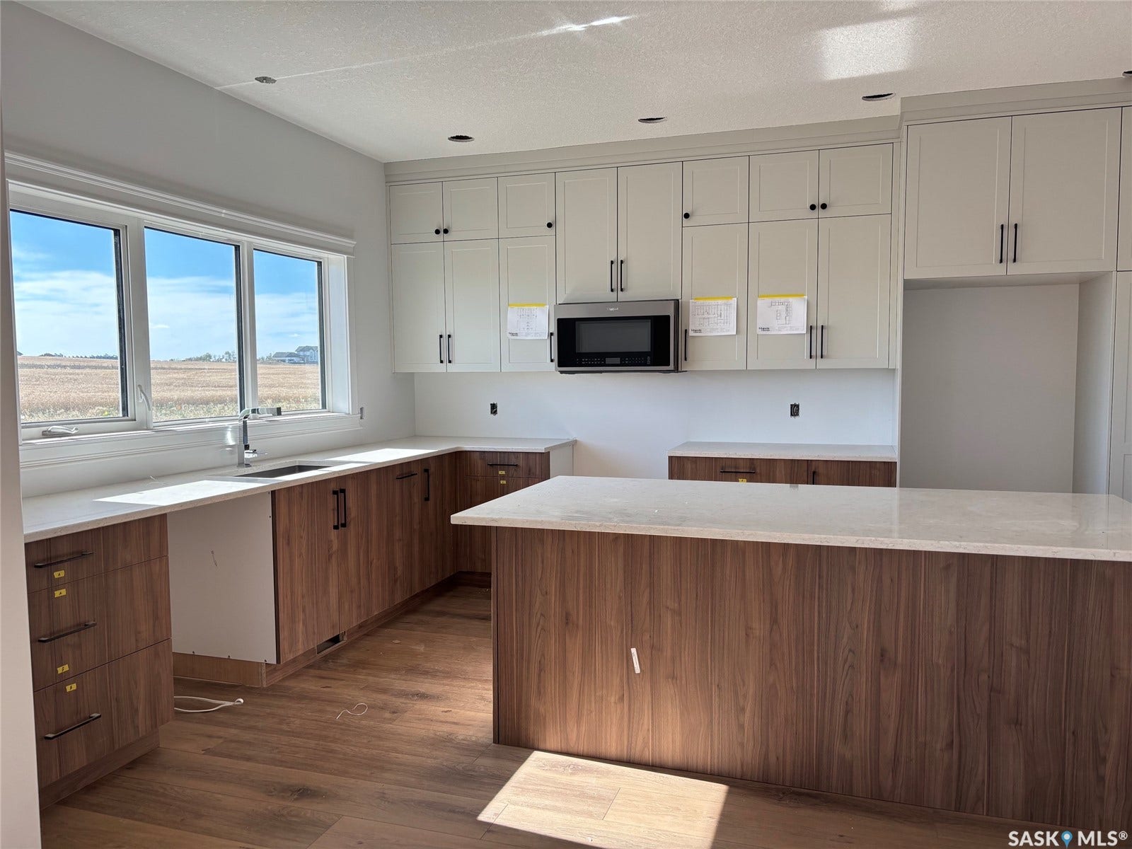 Kitchen featuring wood-finish lower cabinetry, light-toned upper cabinetry, a central island with a light countertop, recessed lighting, and a stainless steel microwave