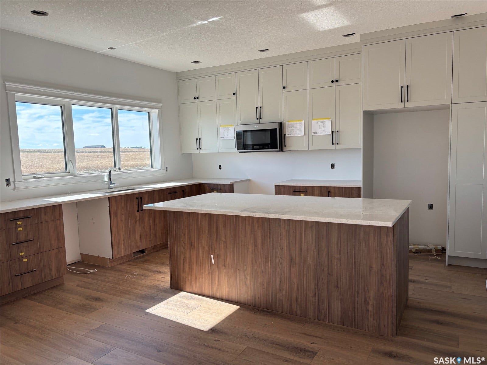 Modern kitchen featuring a central island, light-toned upper cabinetry, wood-finish lower cabinetry, and light countertops