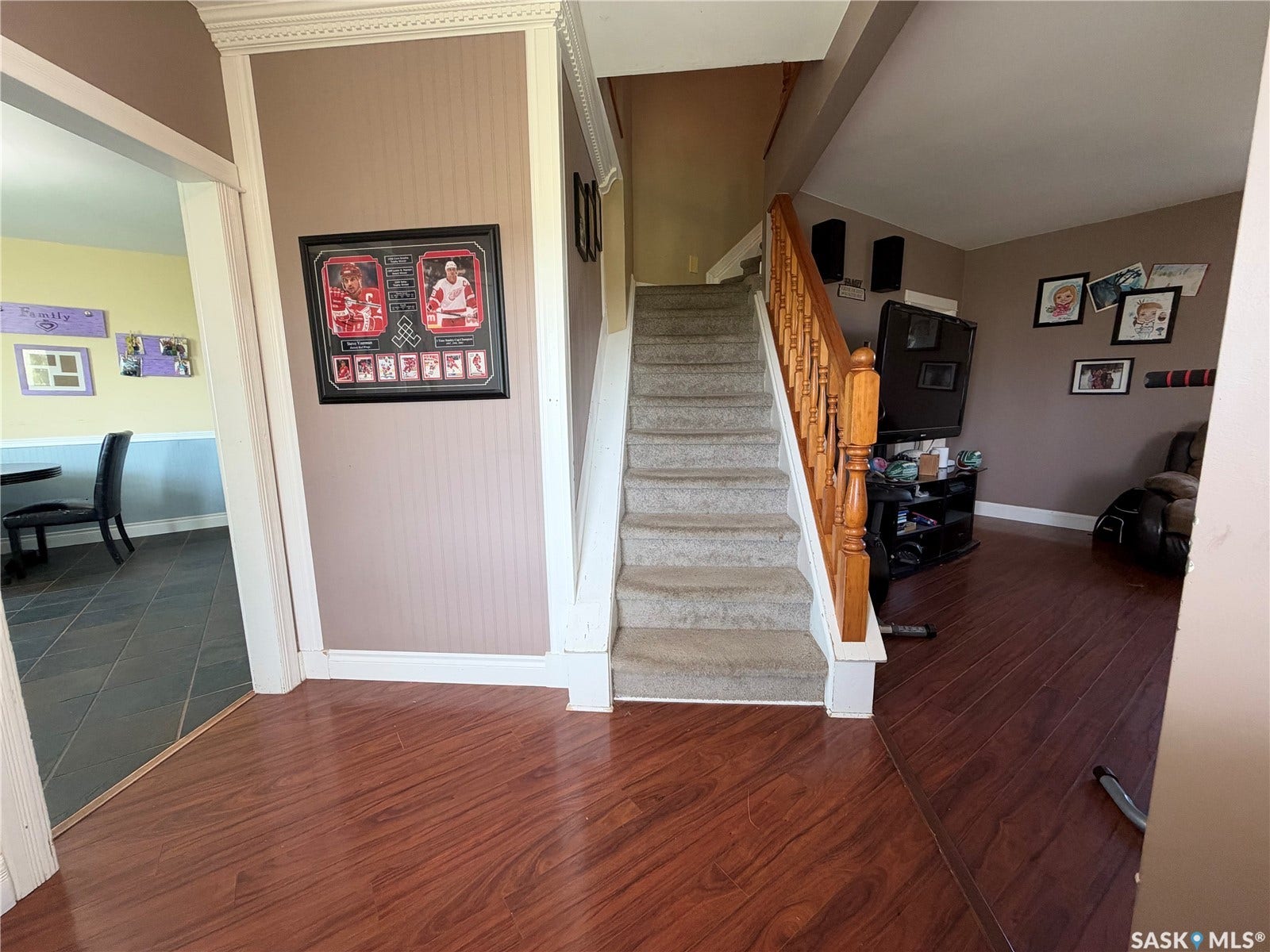 Wood-finish flooring, carpeted staircase, wood banister, crown molding, and a doorway opening to an additional room