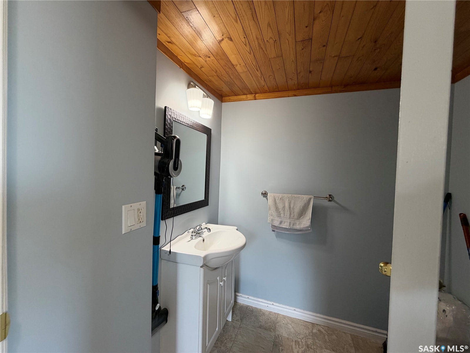 Wood-finish ceiling, vanity with integrated basin, framed mirror, and wall-mounted lighting