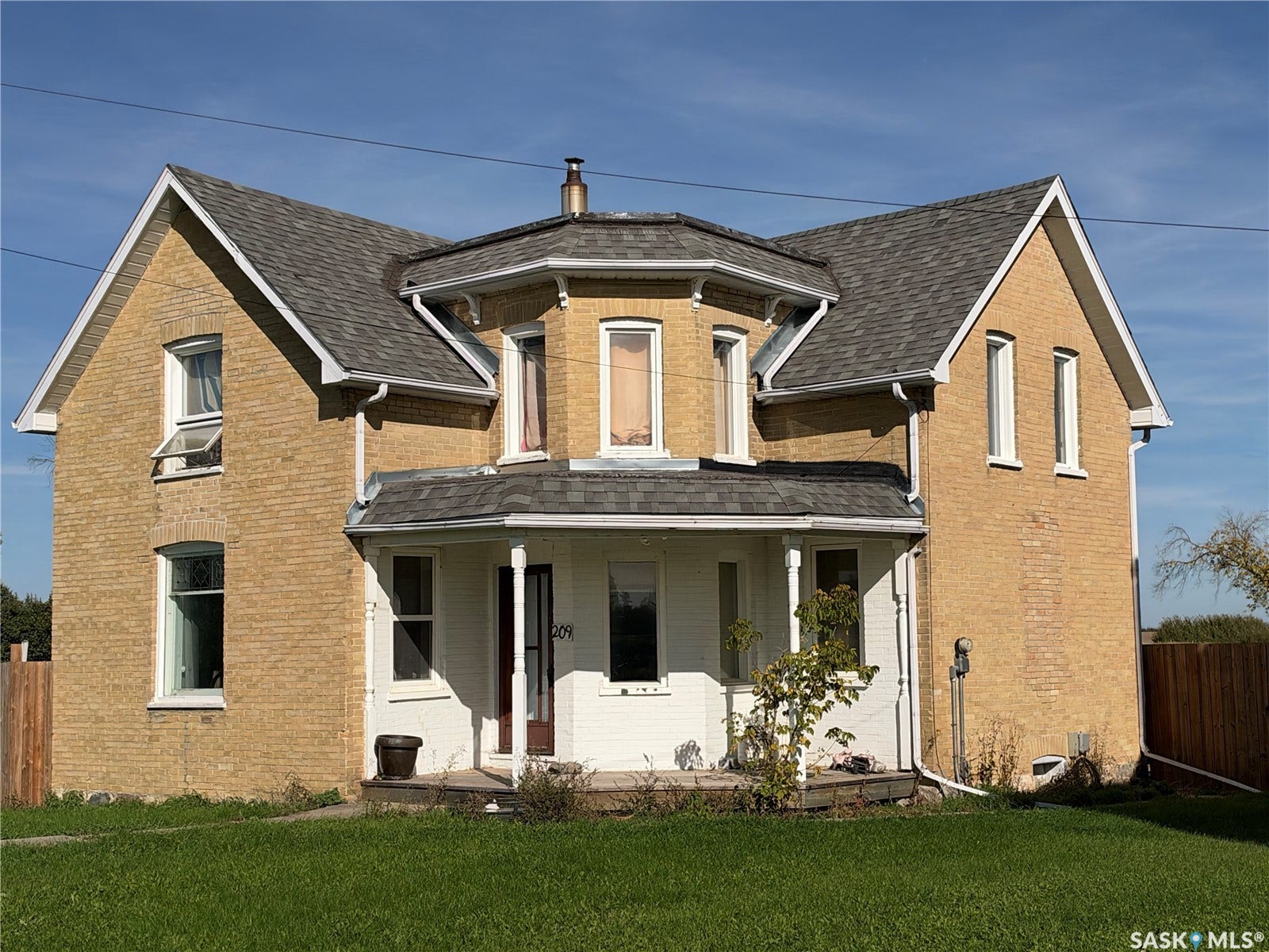 Brick exterior featuring an octagonal second-story projection, front porch with columns, gabled rooflines, and a well-maintained lawn