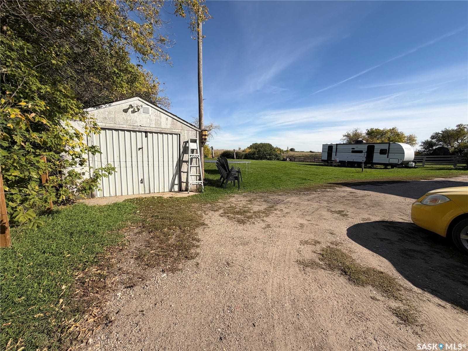 Detached garage with a single bay door, surrounded by a grassy area and a gravel driveway