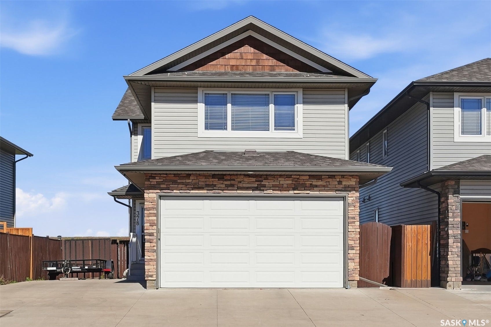 Front elevation featuring light grey siding, stone accents, a single-car garage, and a peaked roofline