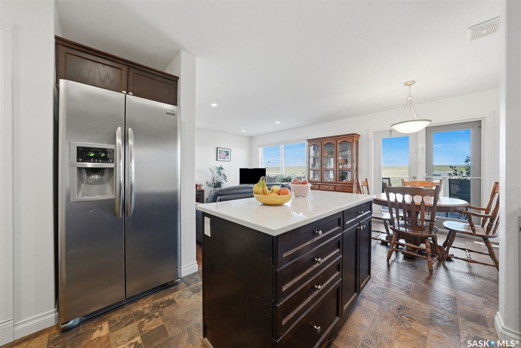 Stainless steel side-by-side refrigerator, dark wood-finish cabinetry, white countertop kitchen island, and wood-finish flooring