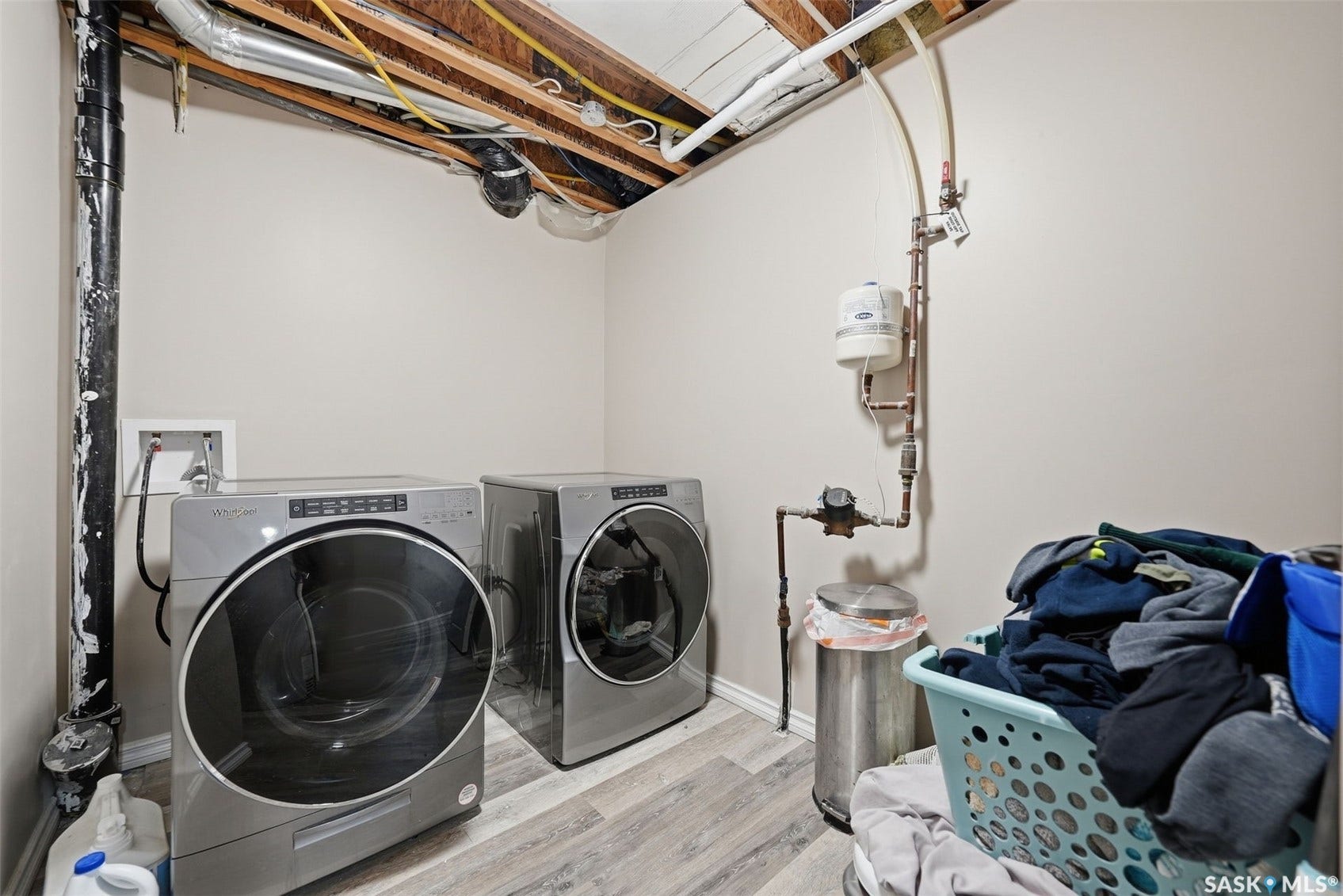 Laundry area with light-toned walls, exposed ceiling joists, and wood-finish flooring