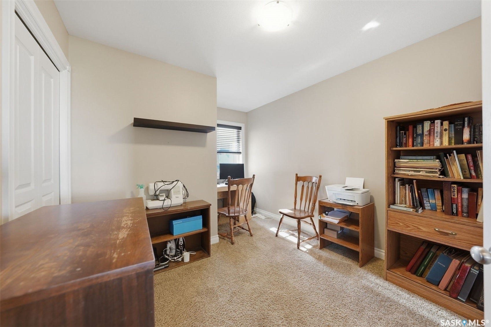 Neutral wall paint, plush carpeting, built-in shelving, window with blinds, and ceiling-mounted lighting