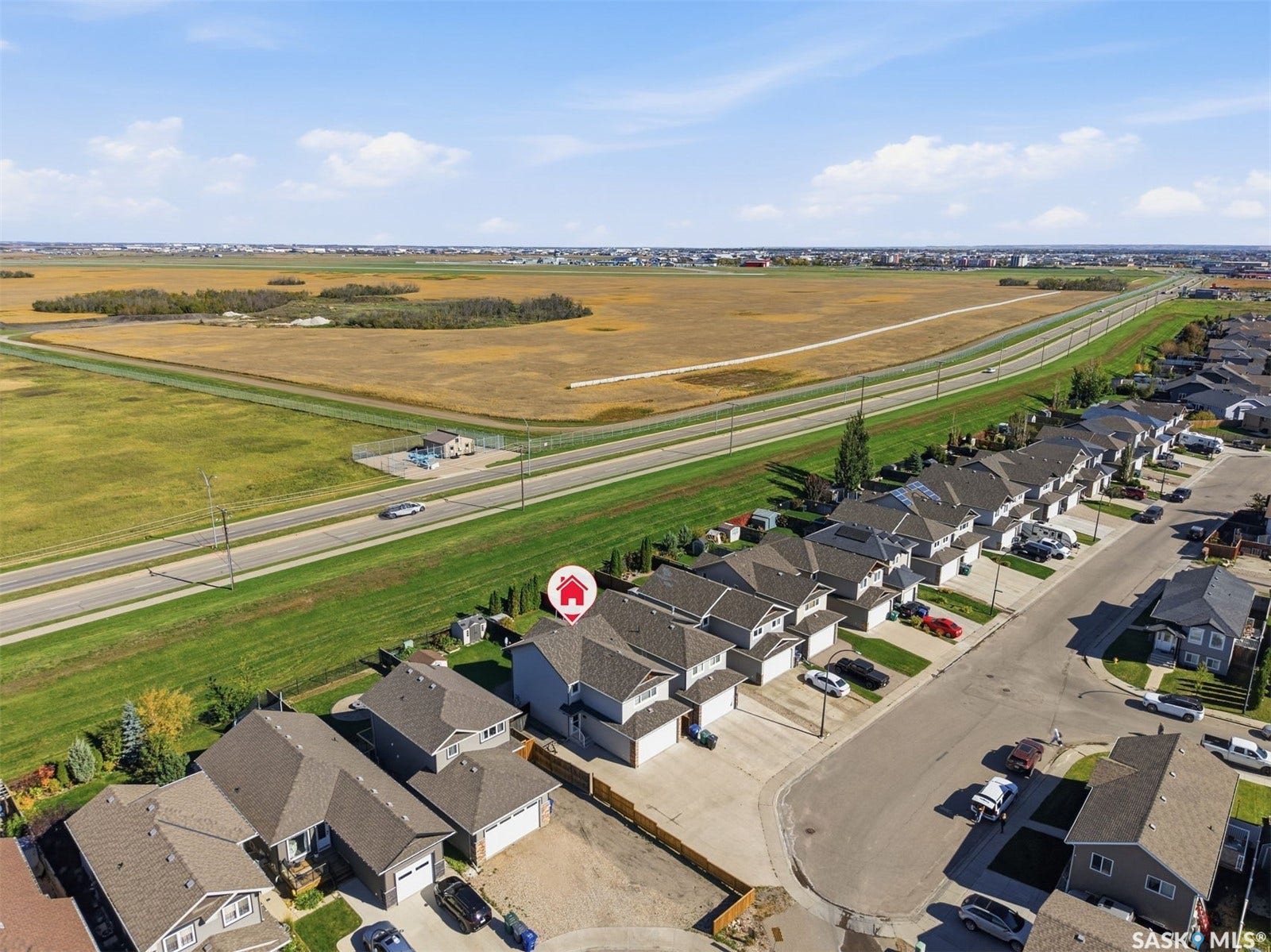 Aerial perspective showcasing a residential development with individual properties, a paved road, and a large expanse of undeveloped land