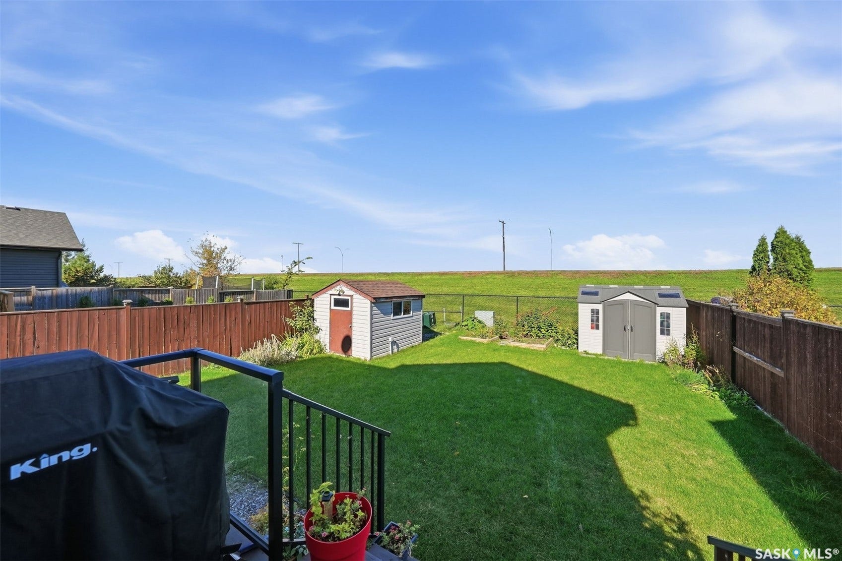 Expansive green lawn with two storage sheds, enclosed by a wood privacy fence