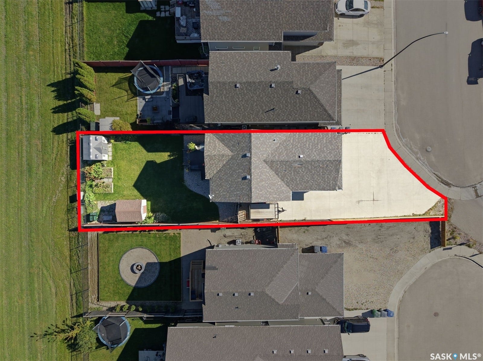 Expansive concrete driveway, attached two-car garage, manicured lawn, and raised garden beds