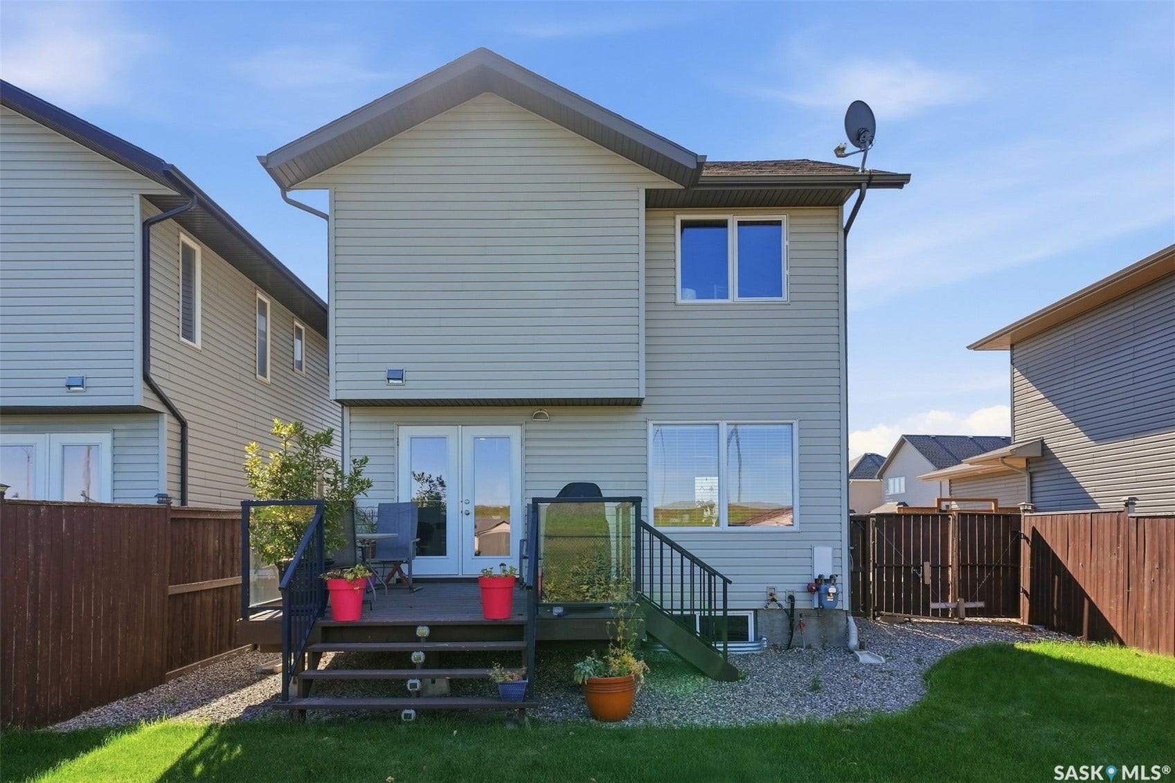 Rear exterior with light-toned siding, a multi-level deck featuring glass panel railings, and a manicured lawn