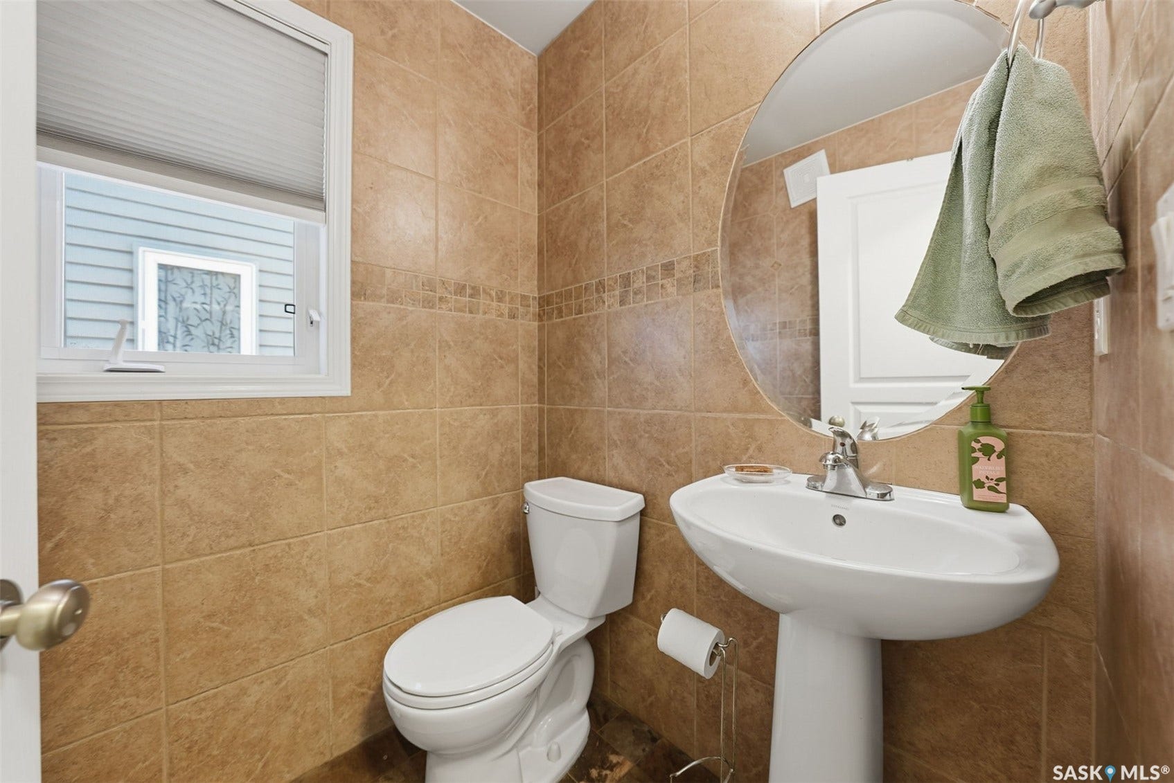 Pedestal sink with chrome faucet, circular wall mirror, and full-height tiled walls featuring a decorative accent band