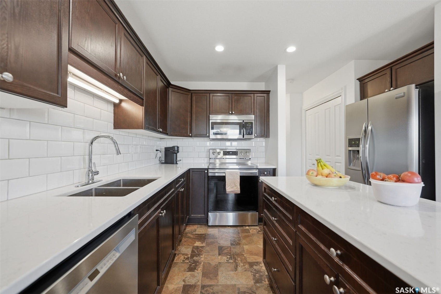 Kitchen featuring rich wood cabinetry, stainless steel appliances, white subway tile backsplash, white countertops, and recessed lighting