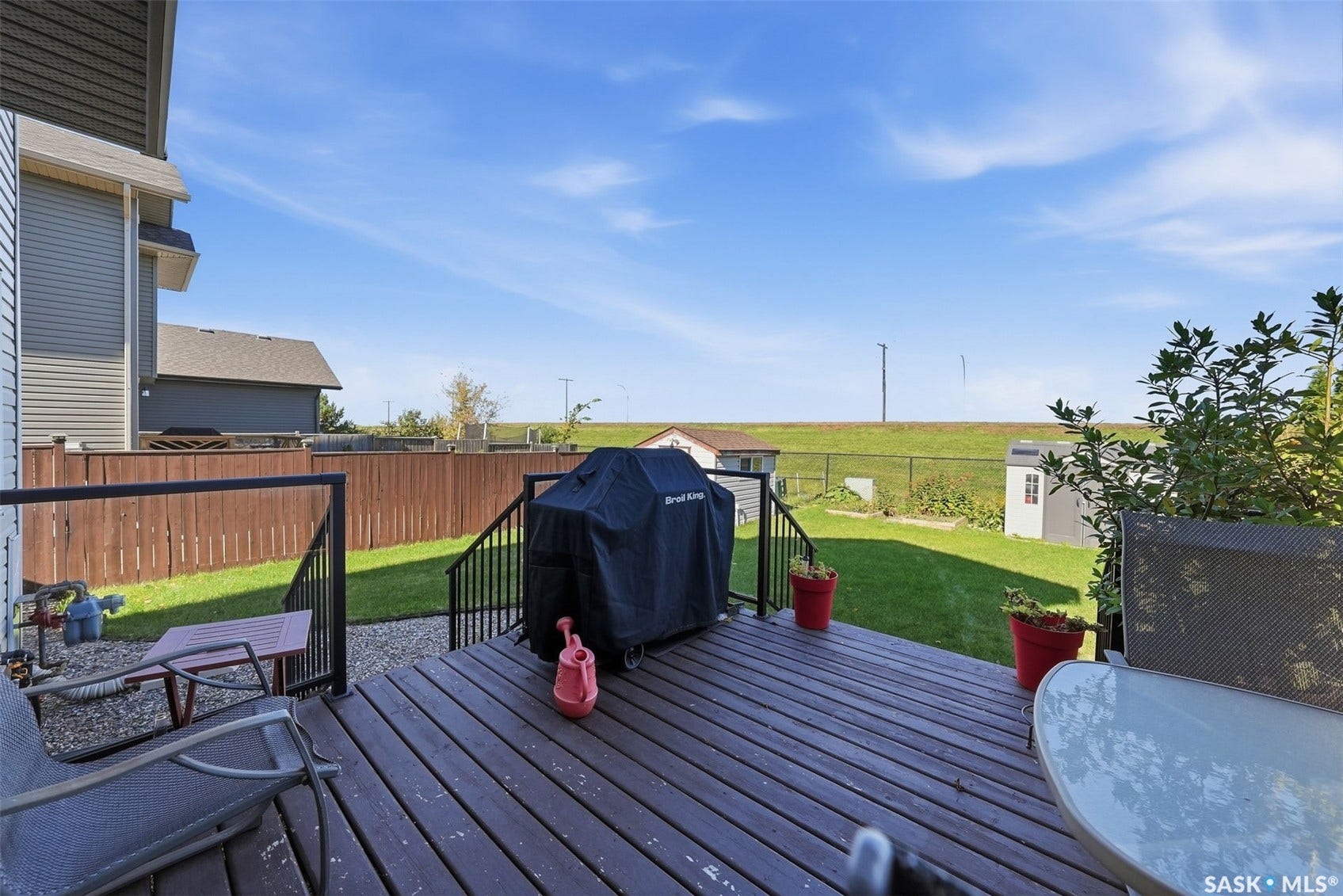 Expansive backyard featuring a wood-finish deck with black railings, a manicured lawn, and two storage sheds
