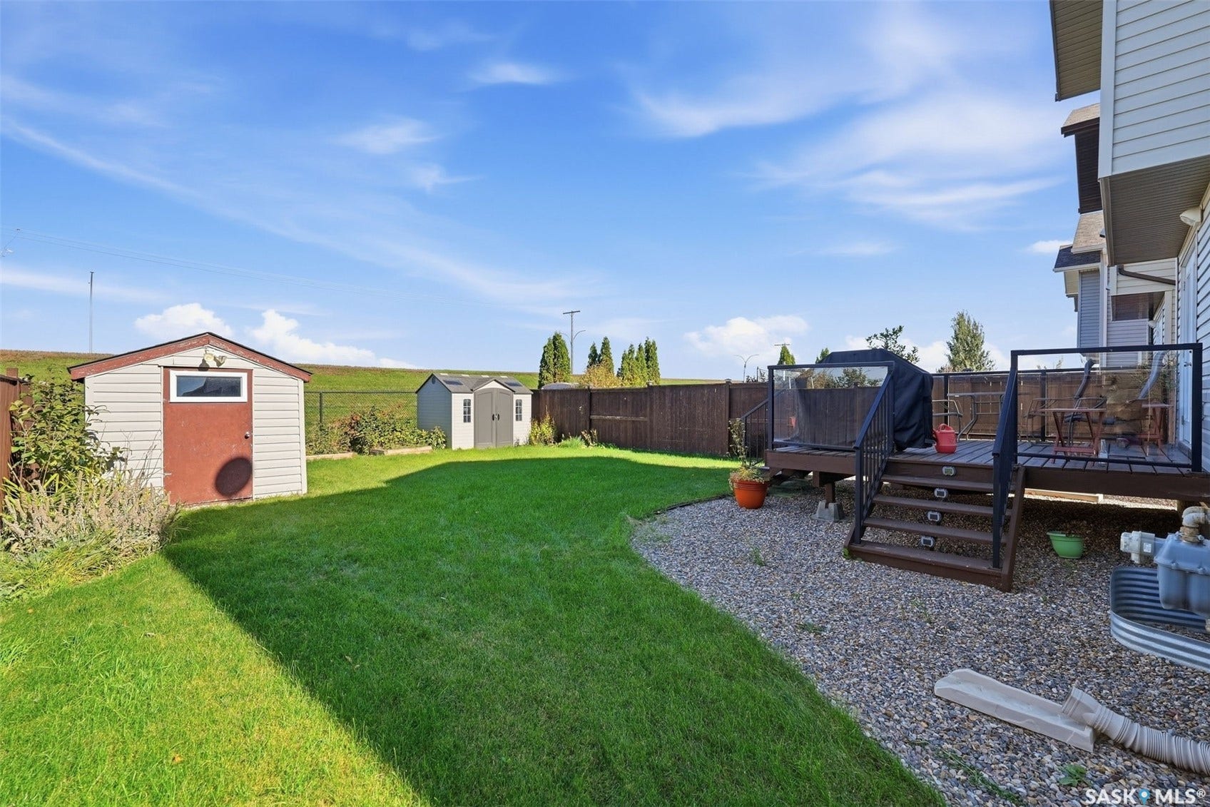 Expansive backyard with a manicured lawn, a wooden deck with glass railings, and a storage shed