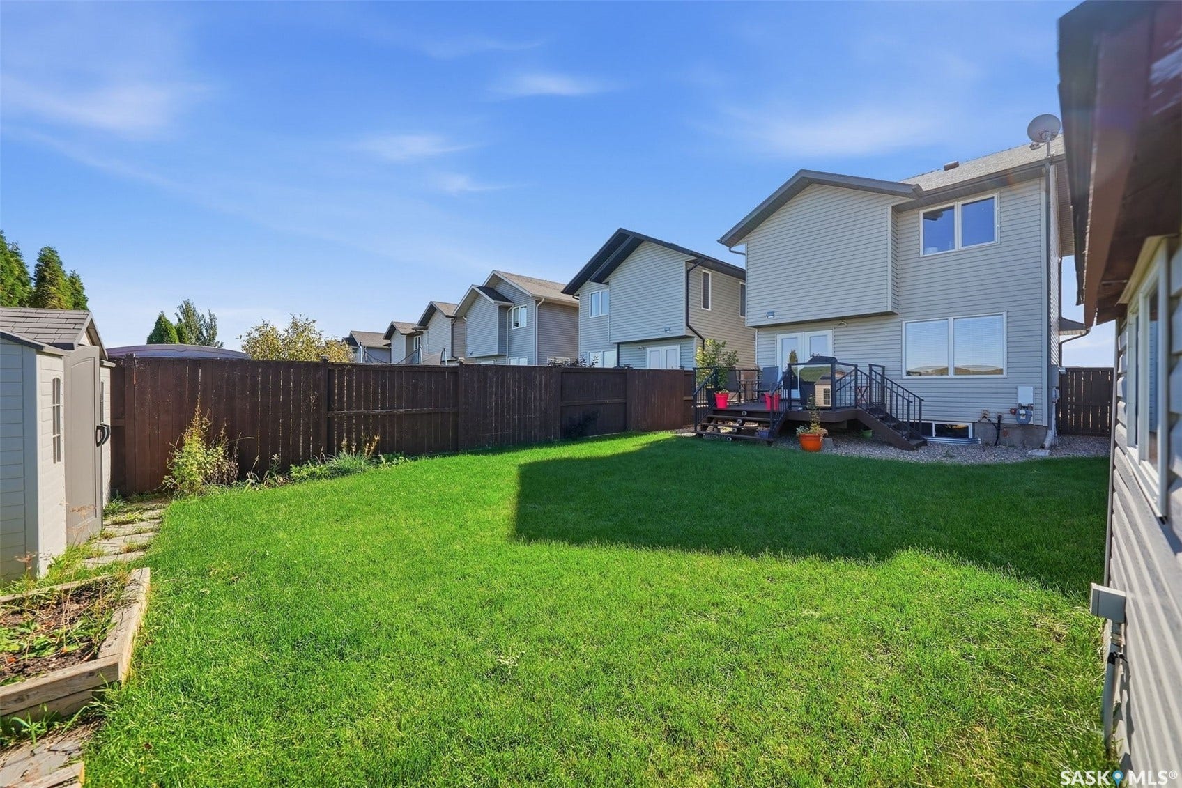 Expansive backyard featuring a green lawn, wood fence, and a multi-level wood deck with dark railings