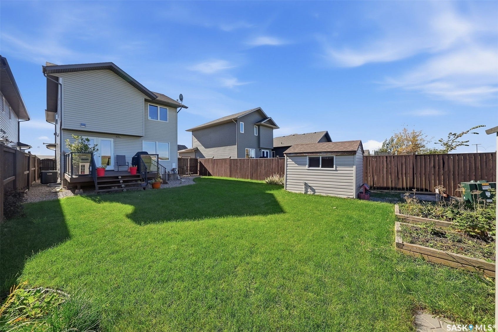 Expansive backyard with a manicured lawn, an elevated deck with glass railing, a storage shed, and a raised garden bed