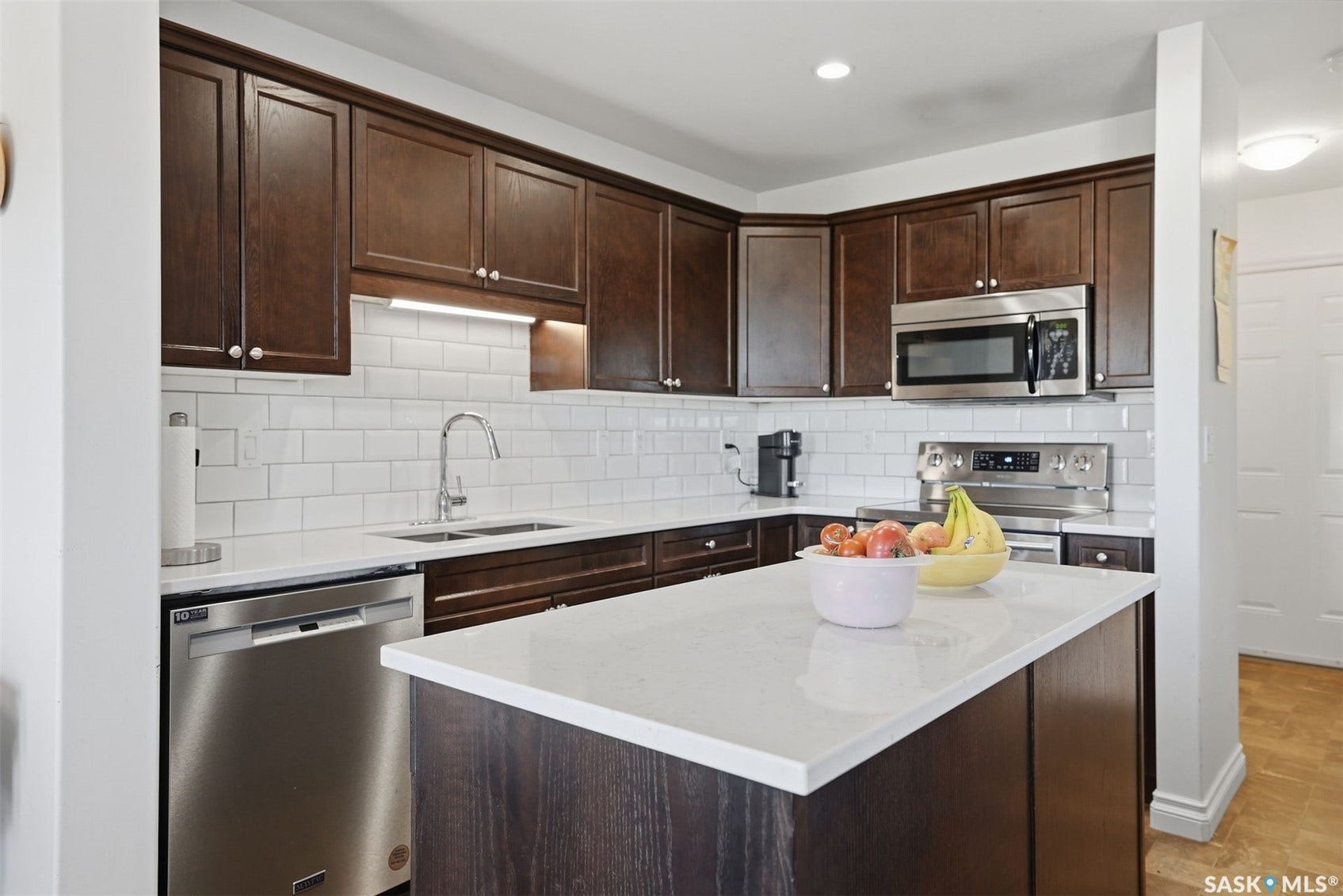 Kitchen featuring dark wood cabinetry, stainless steel appliances, white subway tile backsplash, white countertops, and a central island