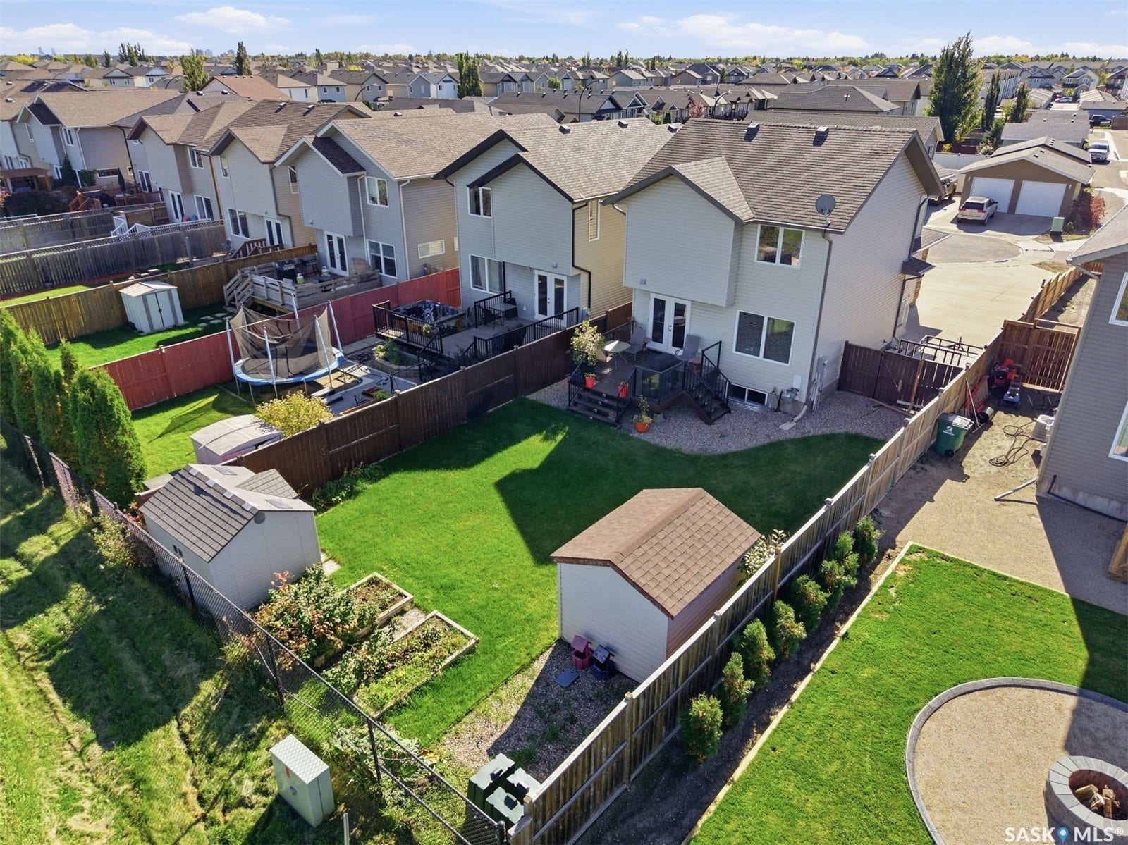 Expansive backyard featuring a manicured lawn, two storage sheds, and a paved area with a fire pit