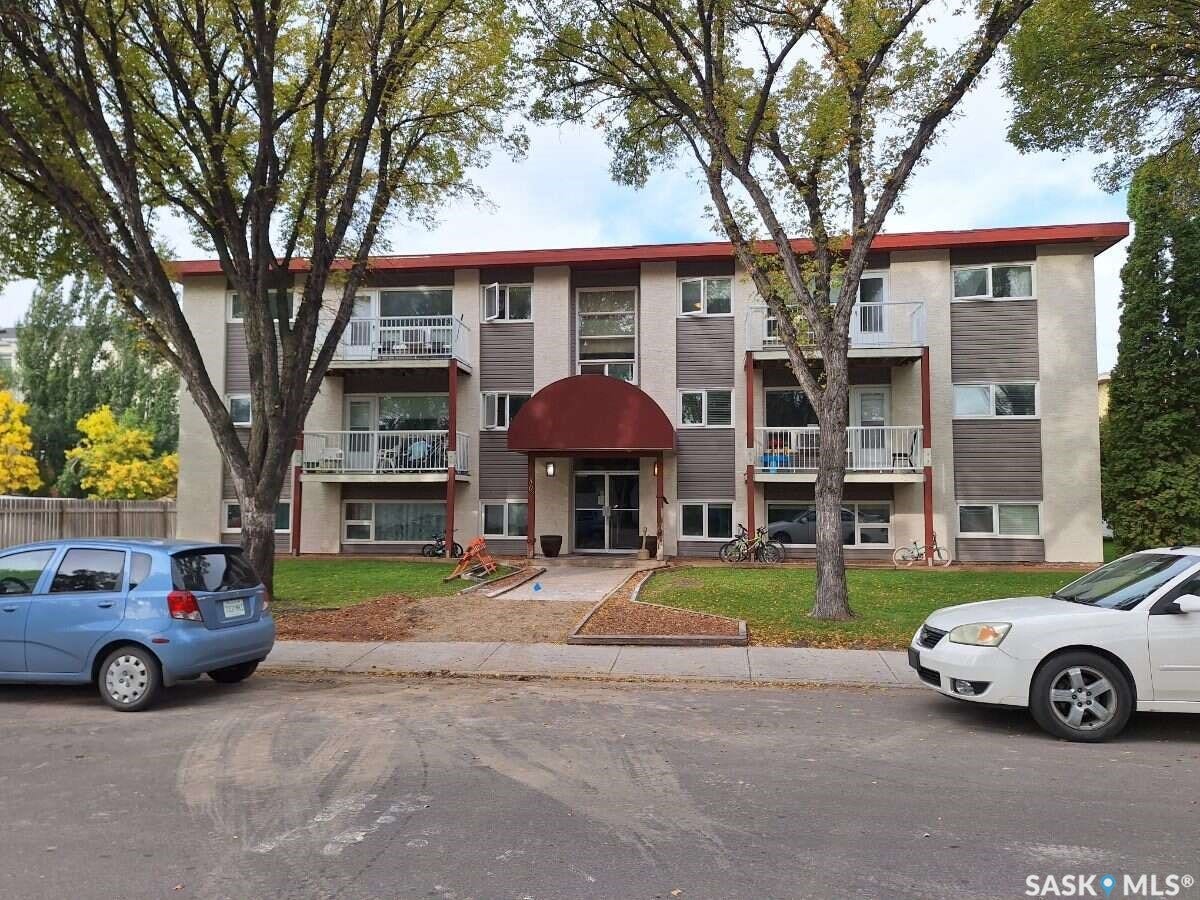 Multi-story building featuring a stucco exterior with horizontal accent panels, individual balconies with white railings, and a prominent red awning over the main entrance
