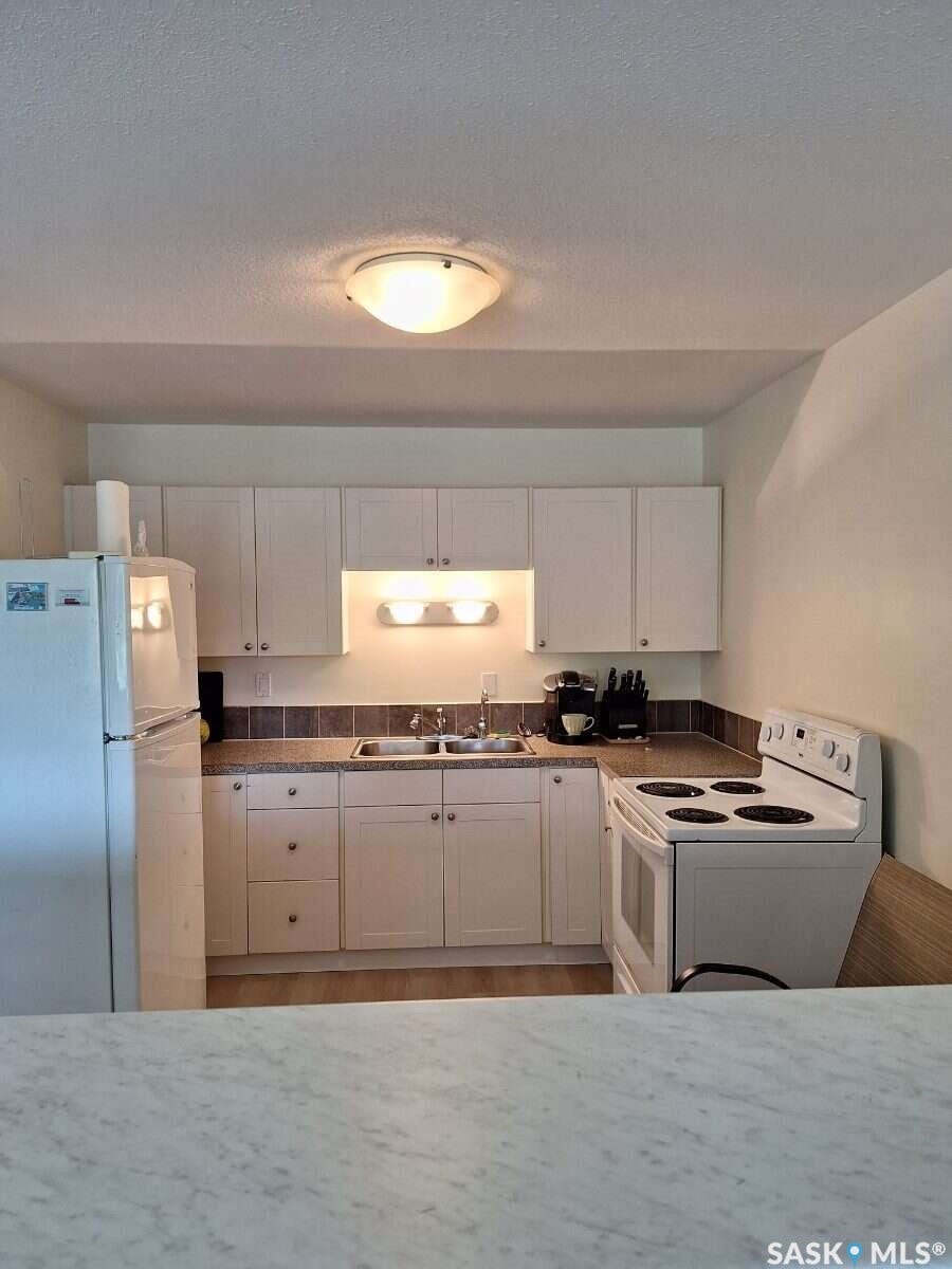Kitchen featuring white cabinetry, a double basin stainless steel sink, dark-toned countertops, and a full-size white electric range