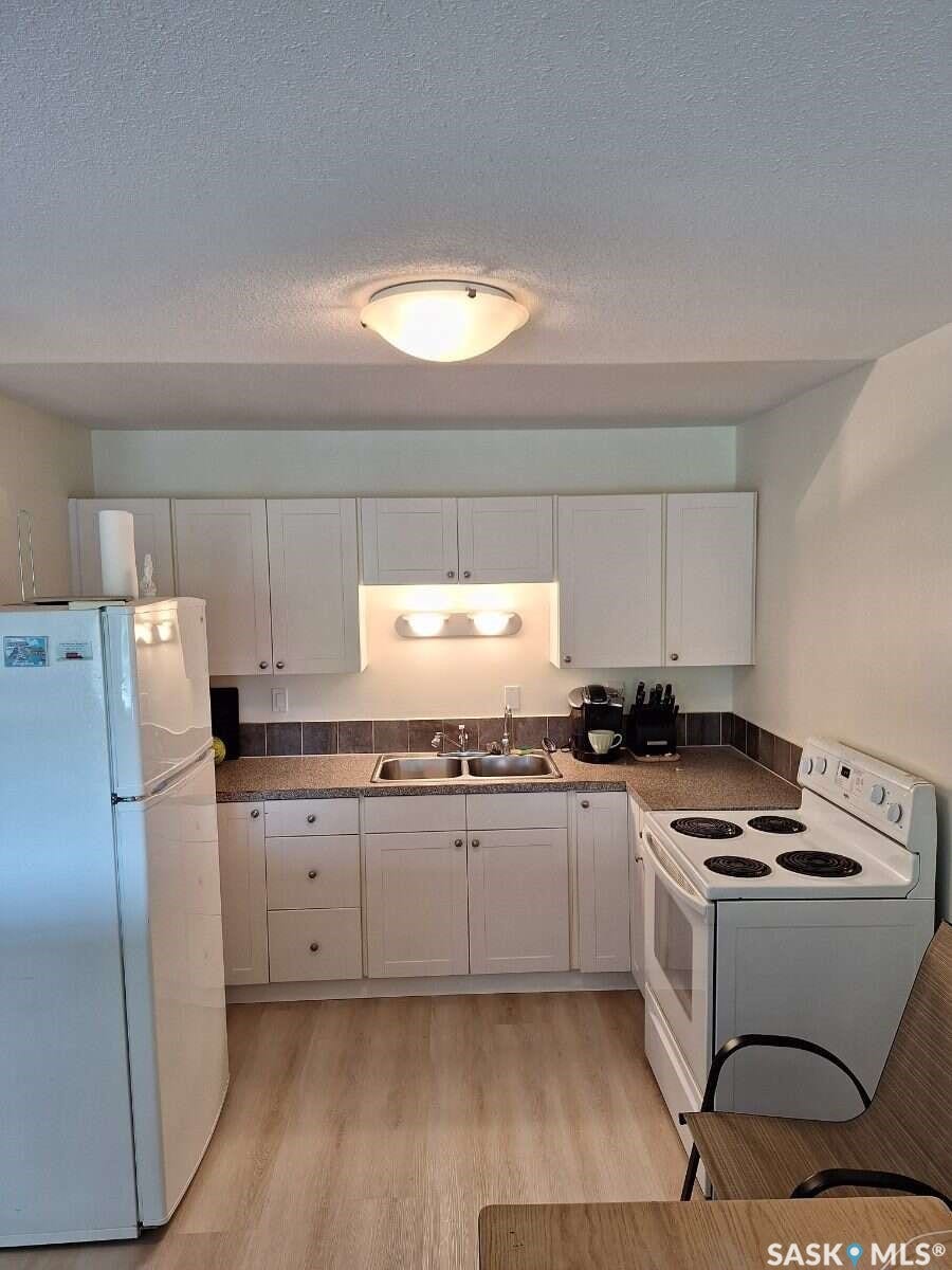 White cabinetry, laminate wood-finish flooring, undermount dual-basin sink, tile backsplash, and a flush mount ceiling light