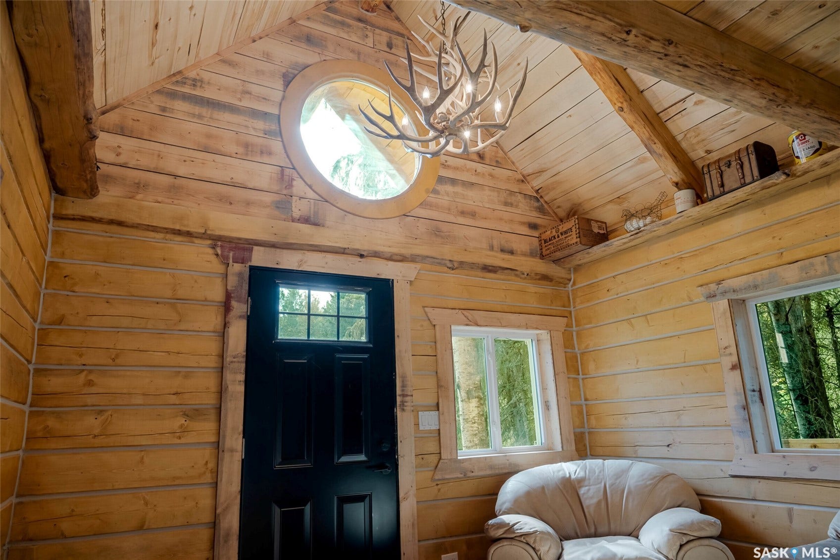 Natural wood-finish walls and vaulted ceilings featuring exposed beams, a round window, and a dark paneled door with lites
