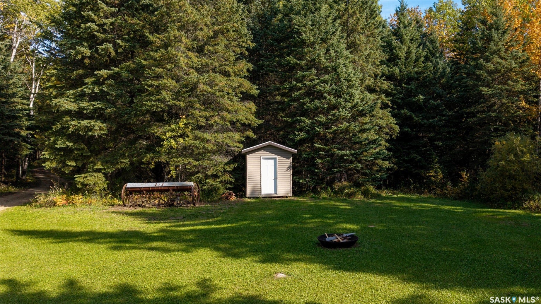 Expansive lawn area with a storage shed, mature trees, and a fire pit