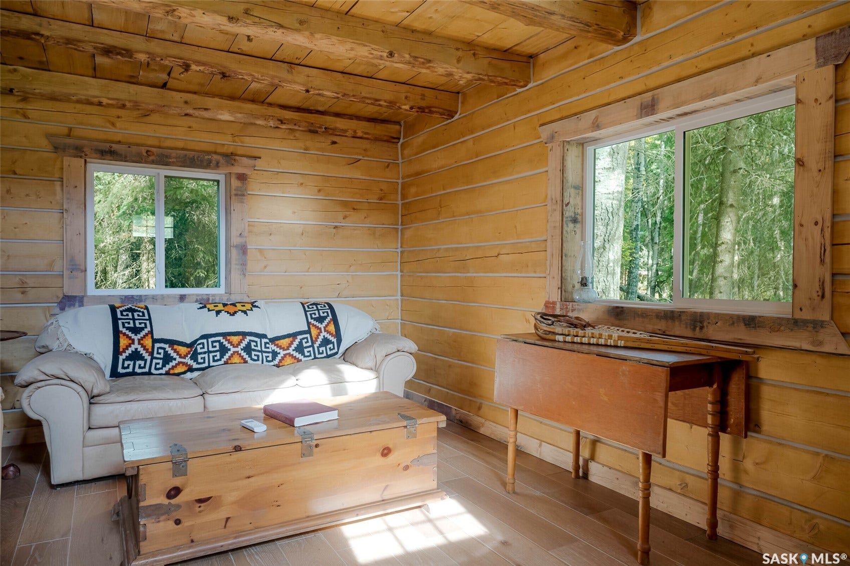 Log cabin interior with exposed wood beams, wood-finish flooring, and two windows with natural wood trim