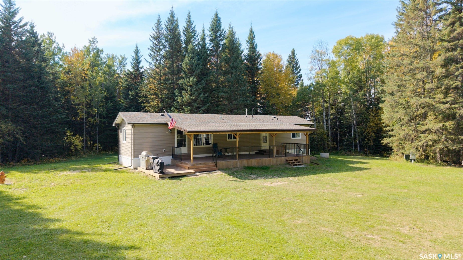 Expansive green lawn surrounding a residence with a covered wood-finish deck and additional wood-finish patio space
