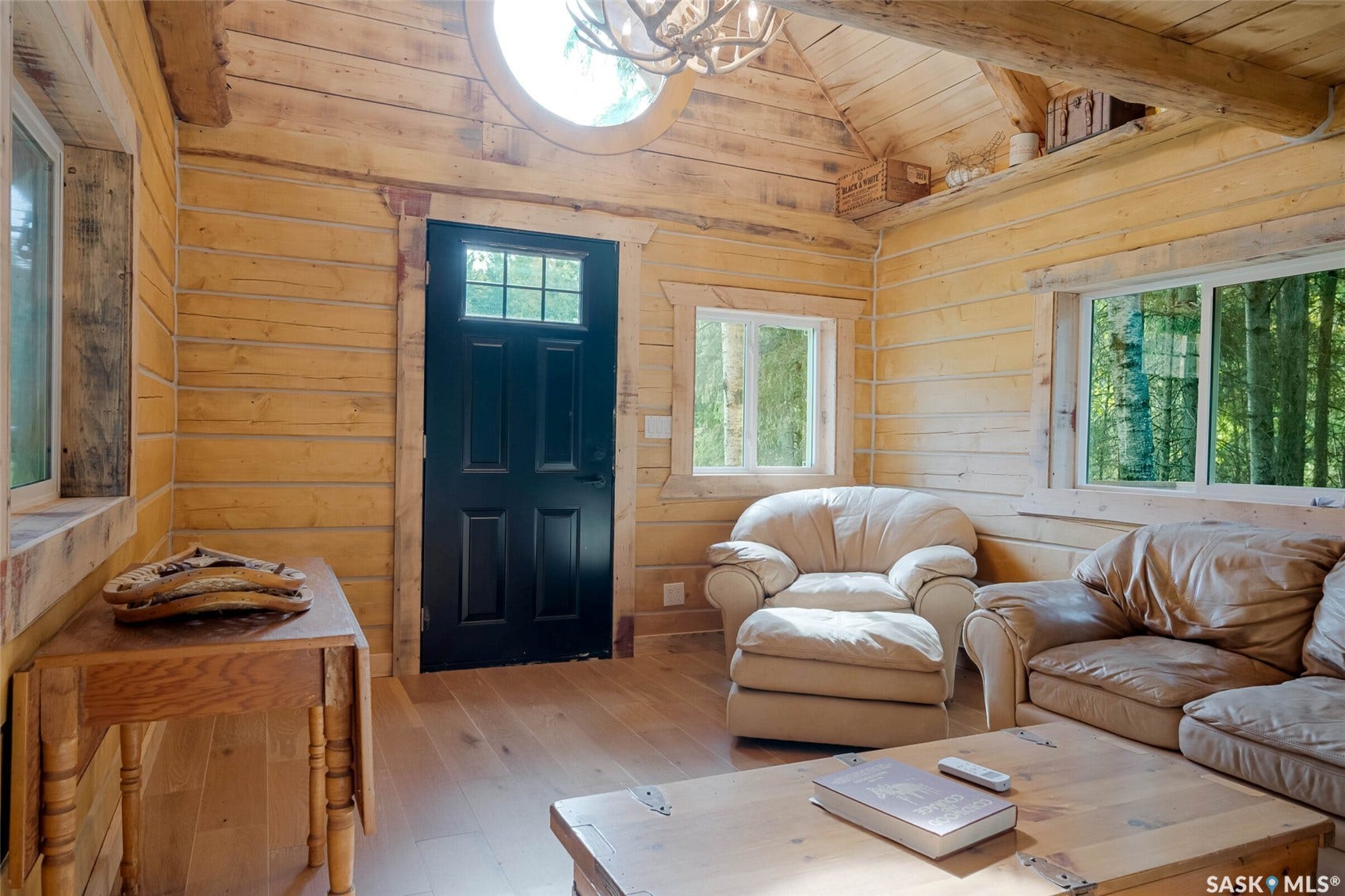 Horizontal wood paneling, wood-finish flooring, multiple windows, and a black paneled door with windowpane detailing