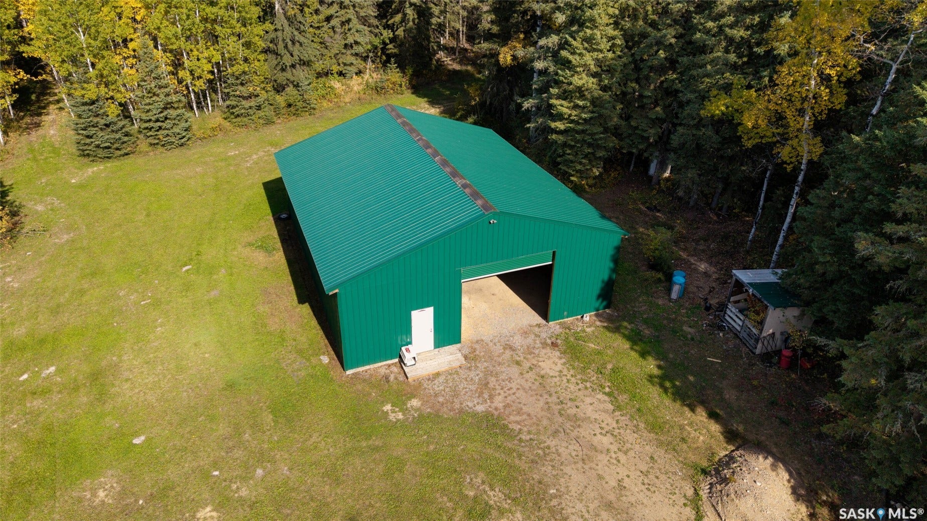 Green metal-sided structure with a gabled roof, large open bay, and a single entry door
