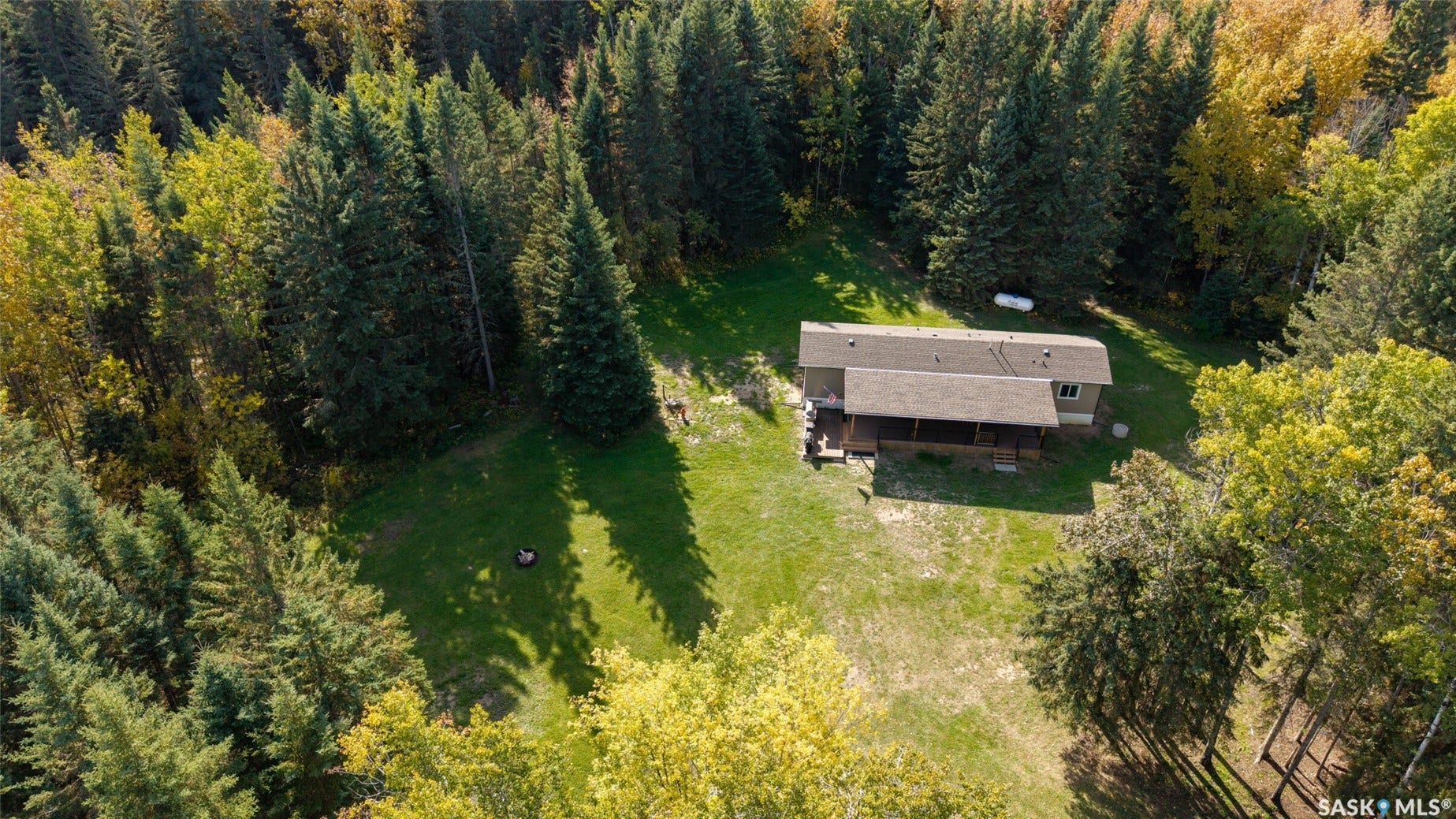 Wooded surroundings with mature trees, expansive grassy areas, and a house featuring a covered porch