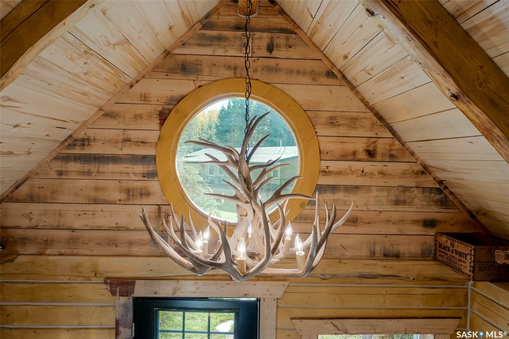 Vaulted wood-paneled ceiling with exposed beams, round window, and decorative antler chandelier