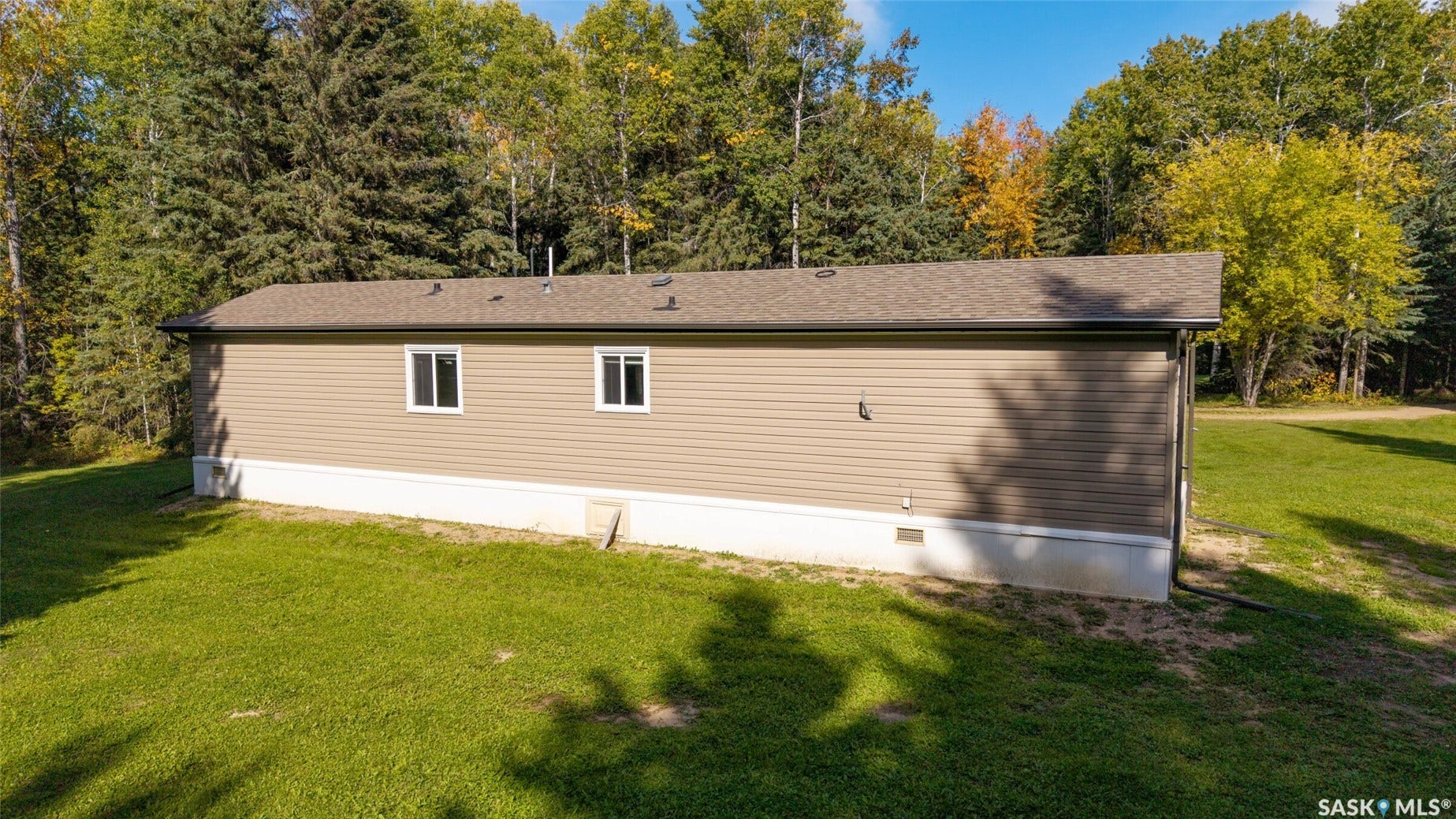 Tan horizontal siding exterior with a brown shingle roof, white trim windows, and a foundation skirt