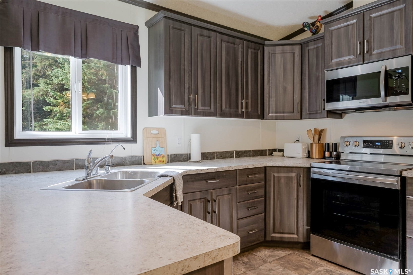 Kitchen featuring wood-finish cabinetry, light-toned countertops, tile flooring, and stainless steel appliances