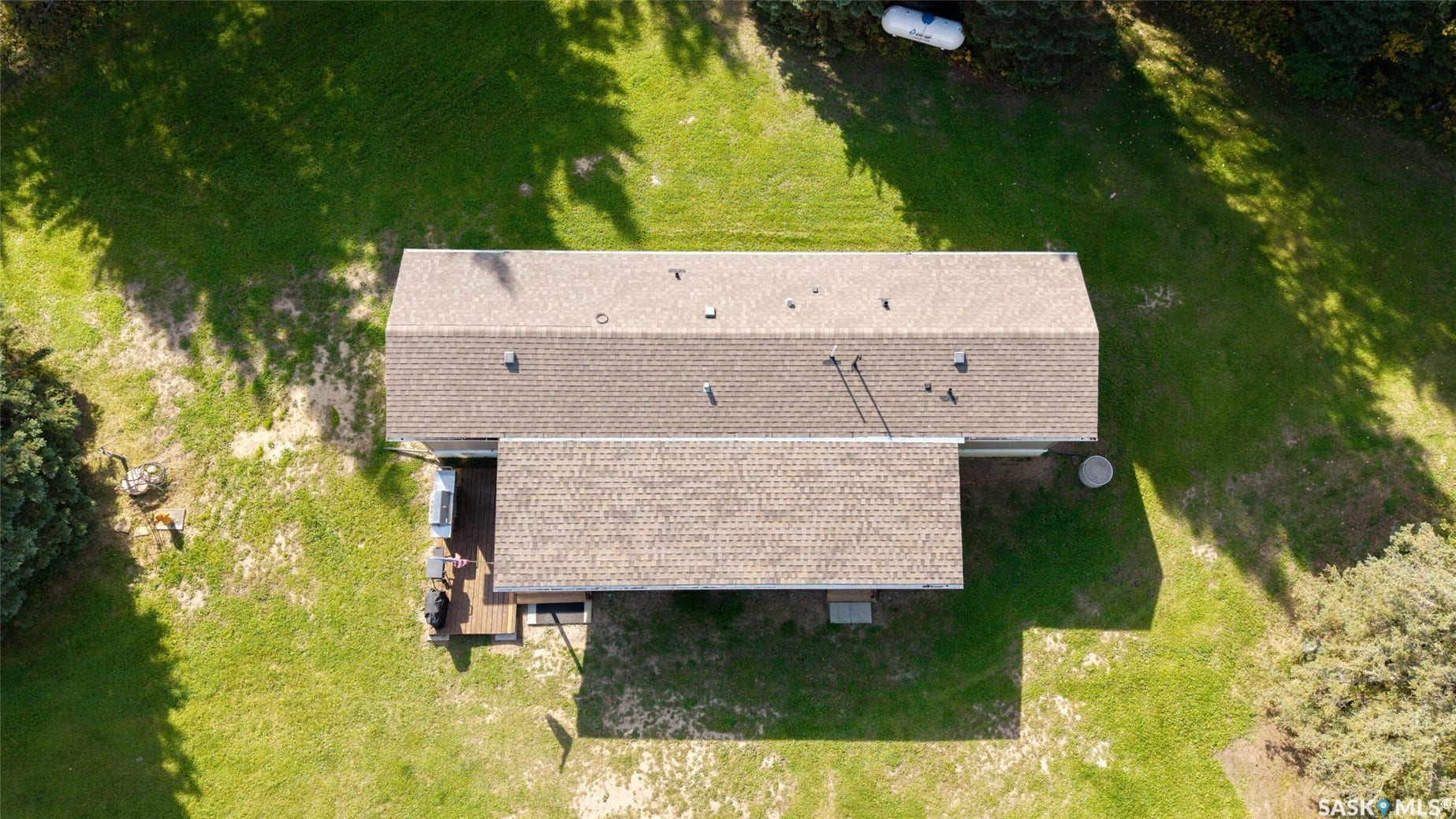 Expansive property featuring a brown shingle roof, a rear wooden deck, and surrounding green landscaping