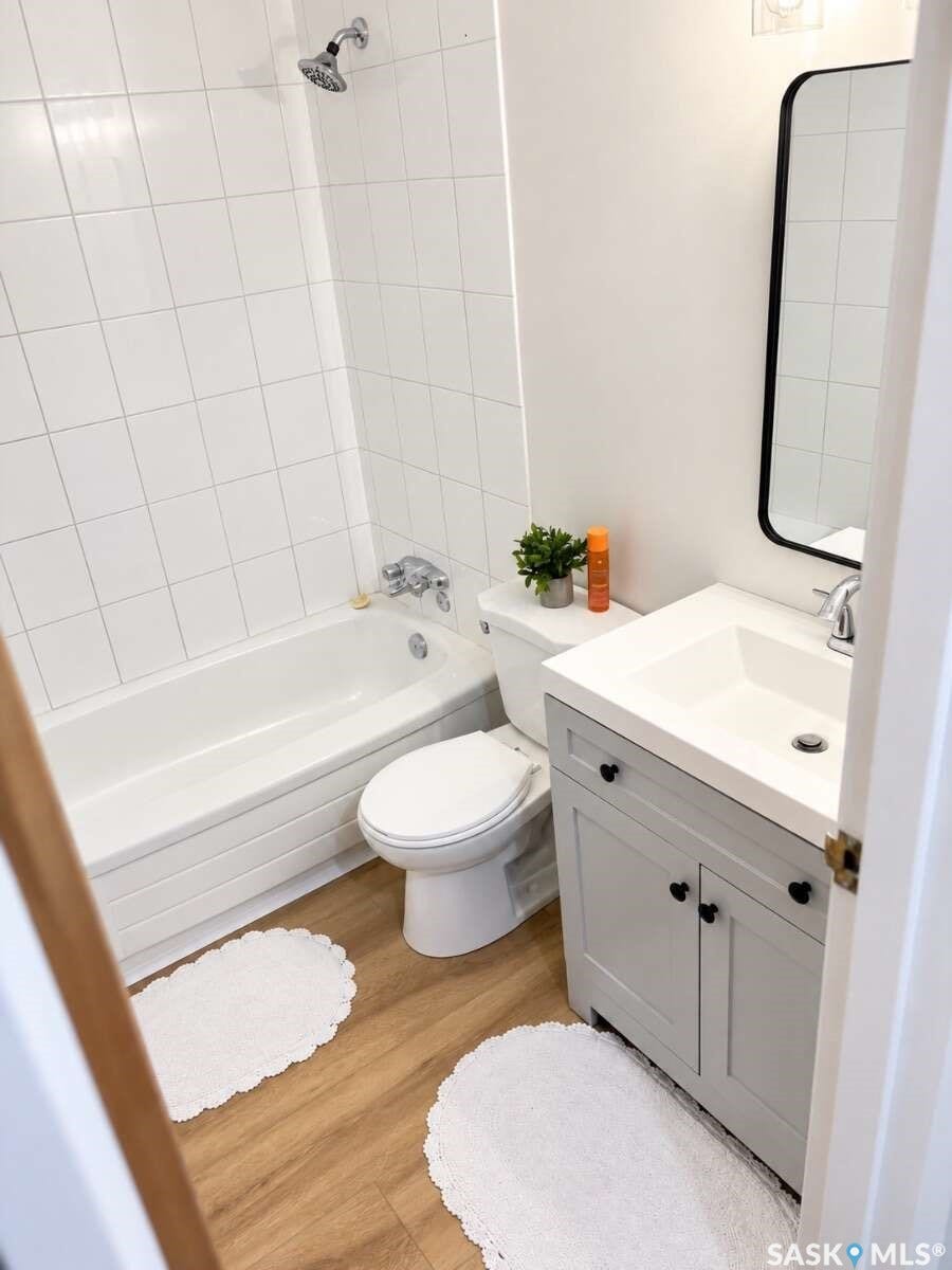 Bathroom featuring a white subway tile tub surround, wood-finish flooring, and a vanity with a rectangular sink and dark hardware