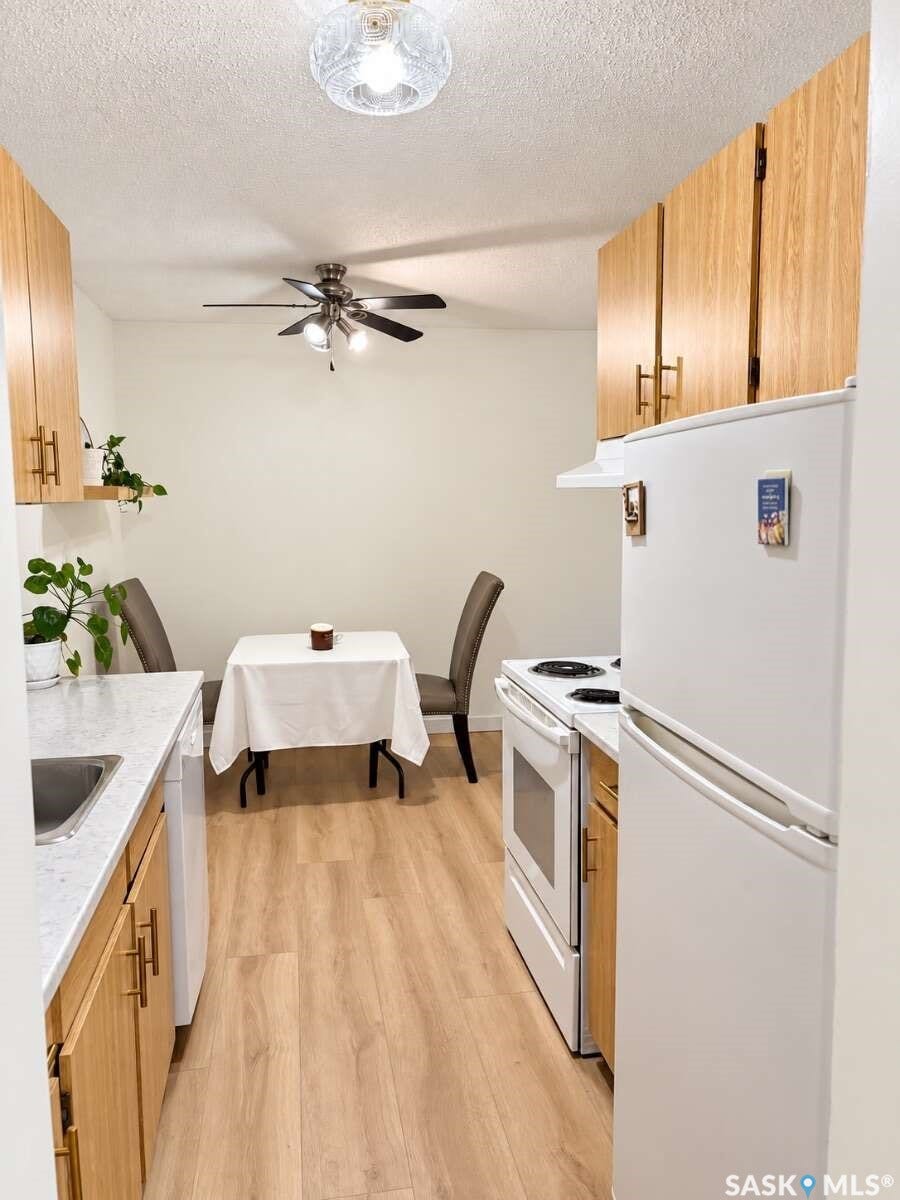 Kitchen with wood-finish flooring, white appliances, and light wood cabinetry with gold-tone hardware