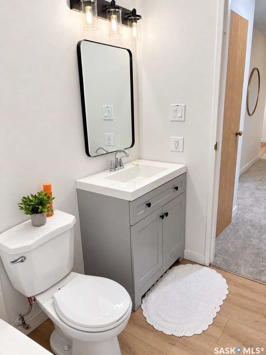 Gray vanity with white countertop, round corner rectangular mirror, light wood-finish flooring, and a white toilet