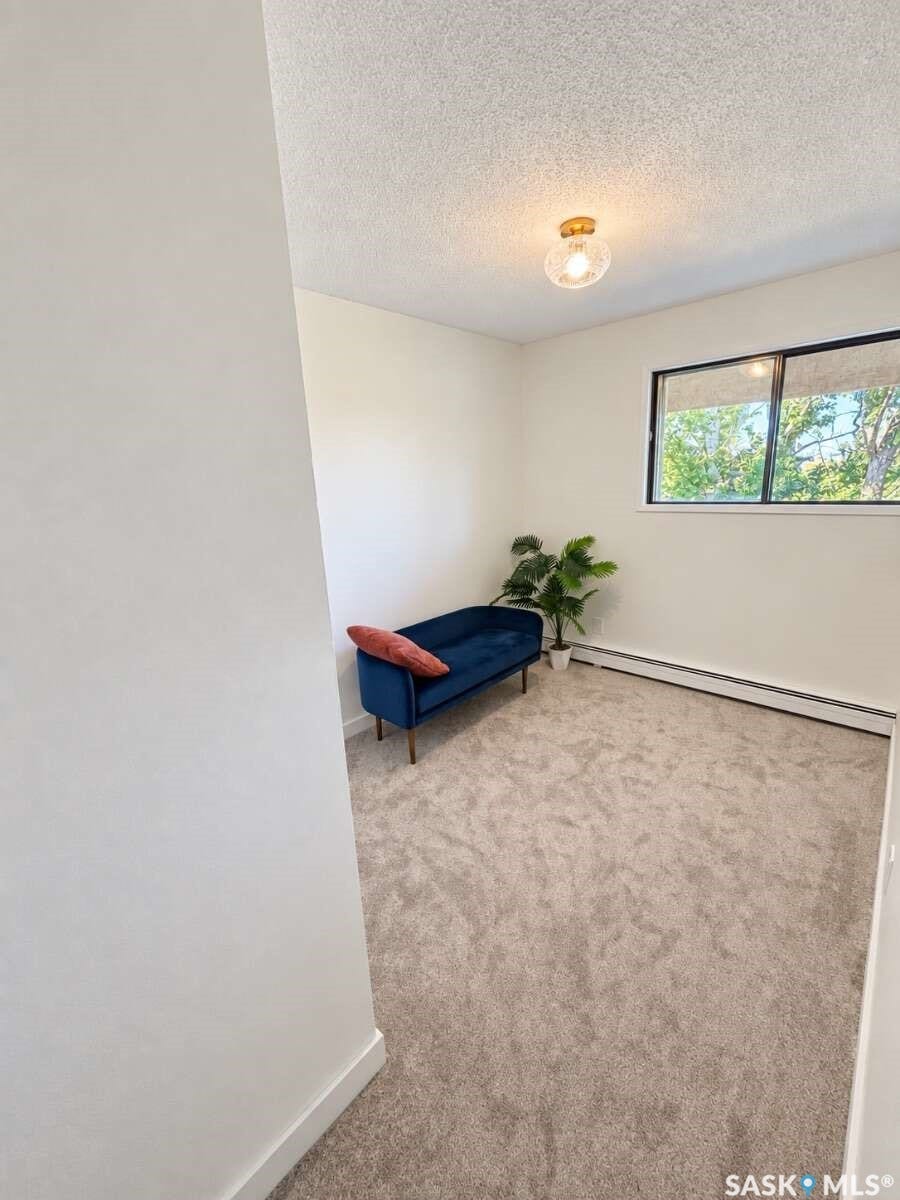 Textured ceiling with a flush-mount light fixture, window with natural light, and carpeted flooring