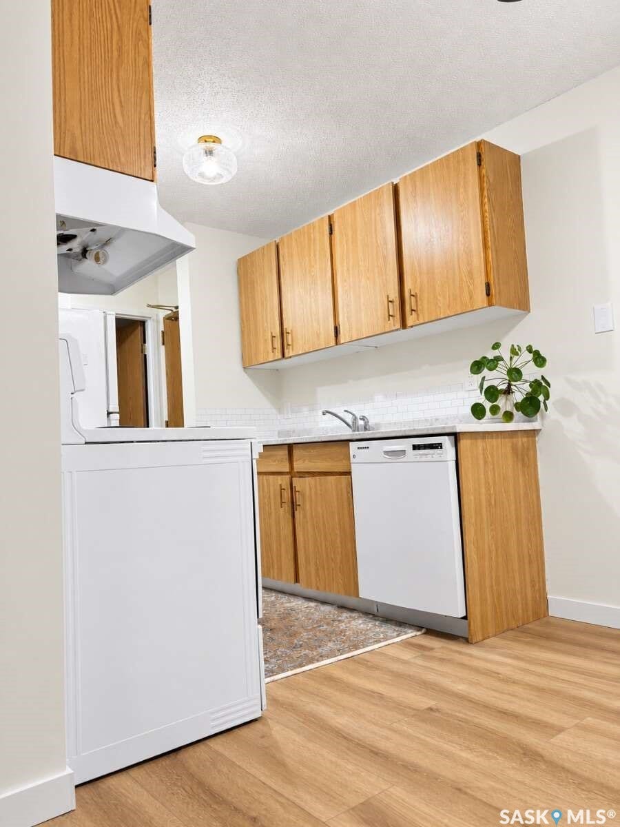Kitchen featuring wood-finish flooring, light wood cabinetry, white subway tile backsplash, and white appliances