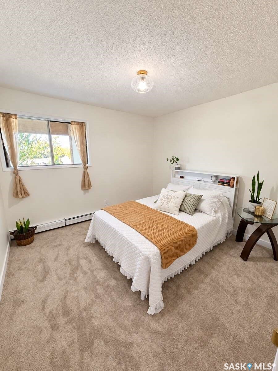 Neutral wall paint, ceiling-mounted light fixture, window with natural light, wall-mounted radiator, and carpeted flooring